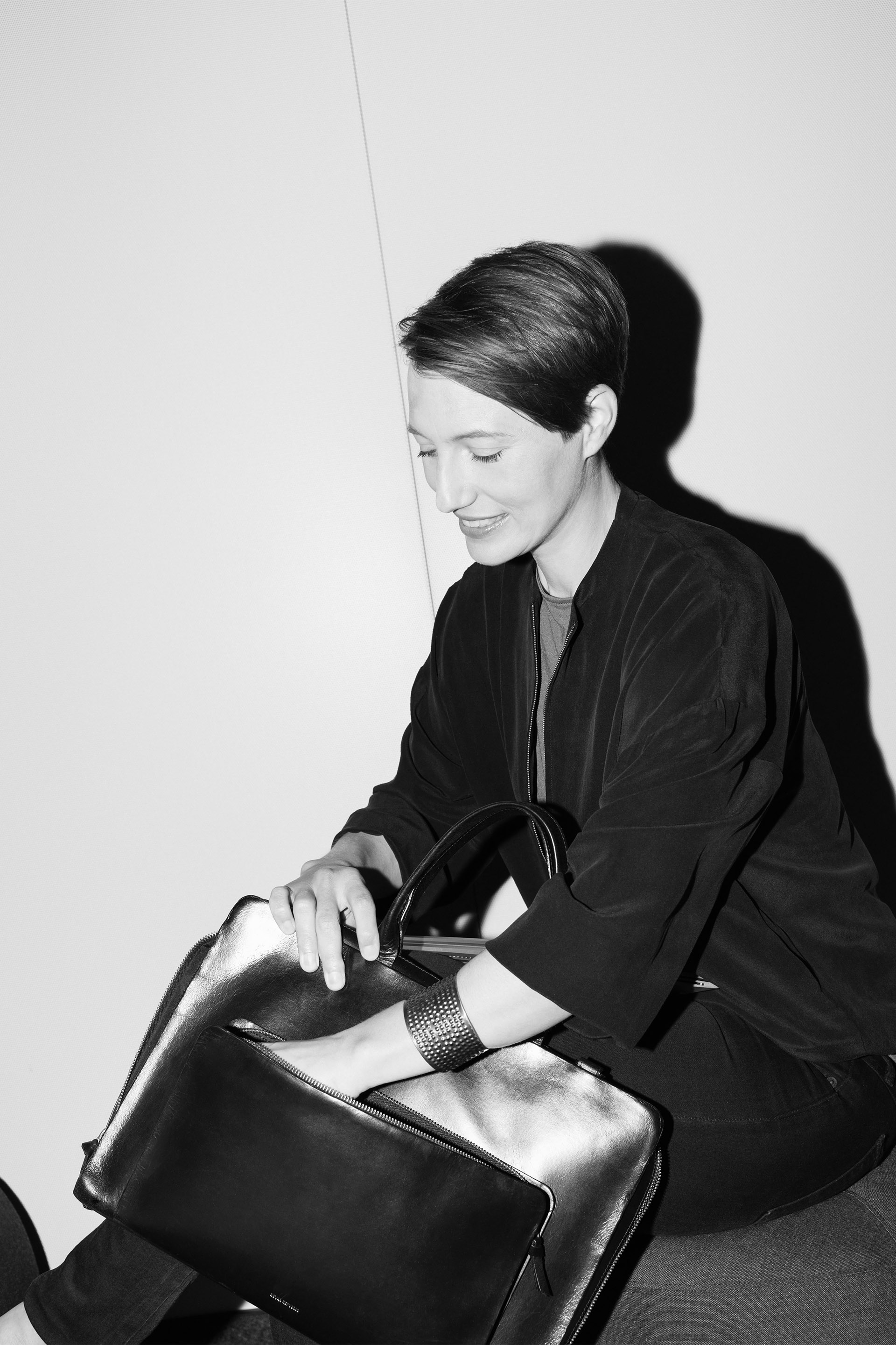 Annegret Maier sits on a chair and reaches into a bag with a smile.