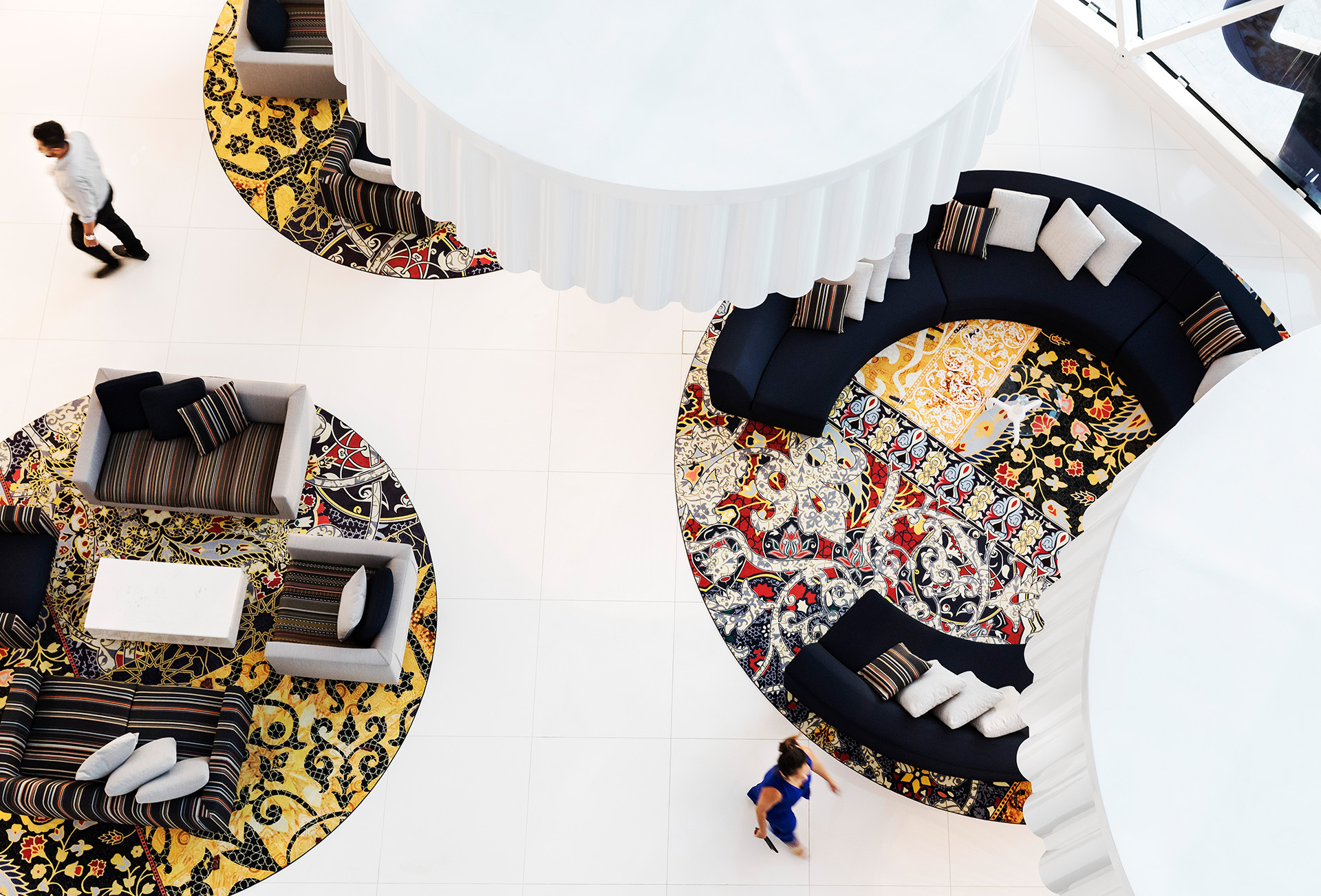 A bird's eye view of a hotel lobby with round, colorful seating islands.